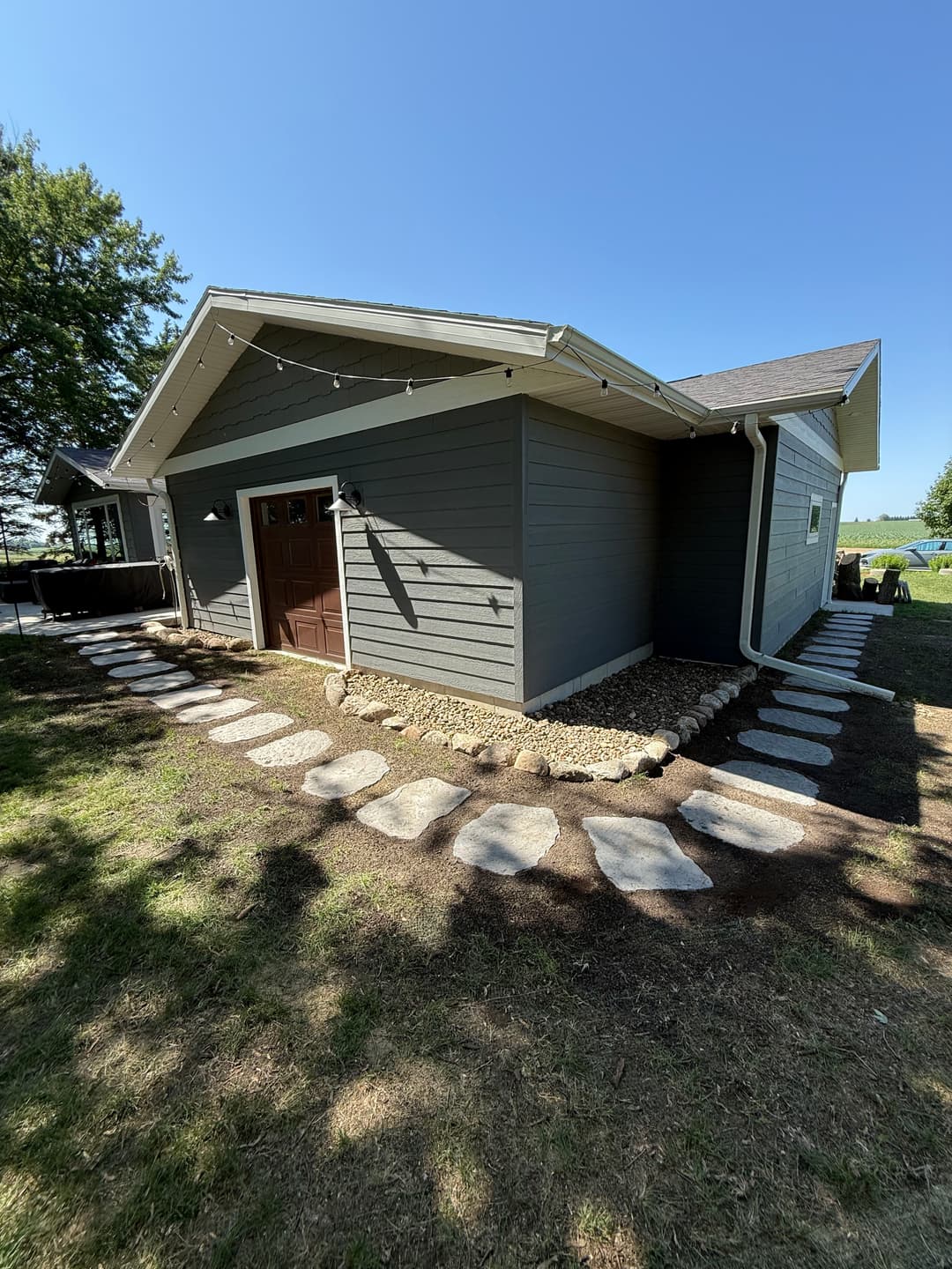 Modern gray house exterior with stone pathway and green lawn under clear blue sky.