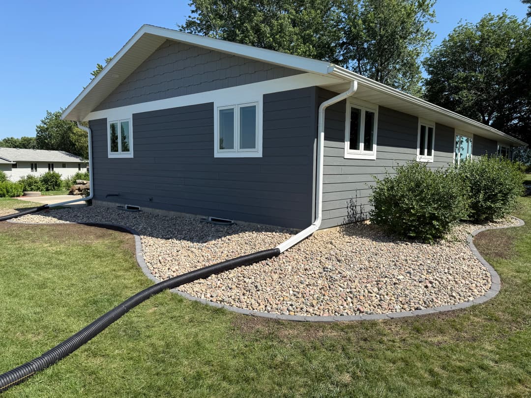 Modern gray home exterior with landscaped yard and drainage system, surrounded by greenery.