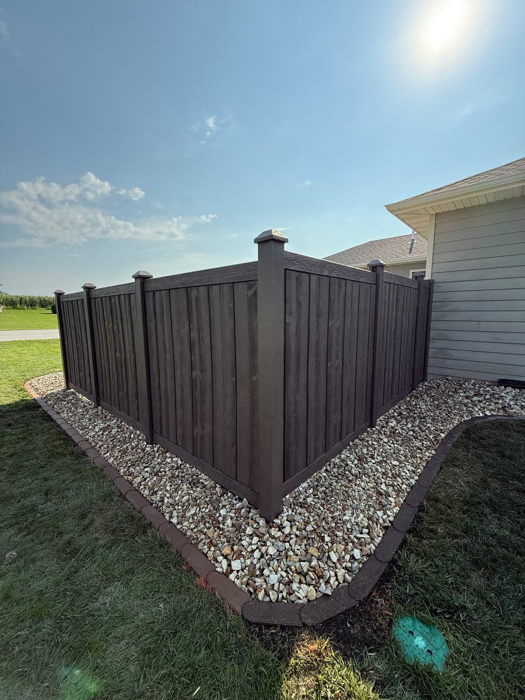 Modern wooden fence with light-colored stone landscaping in a sunny backyard.