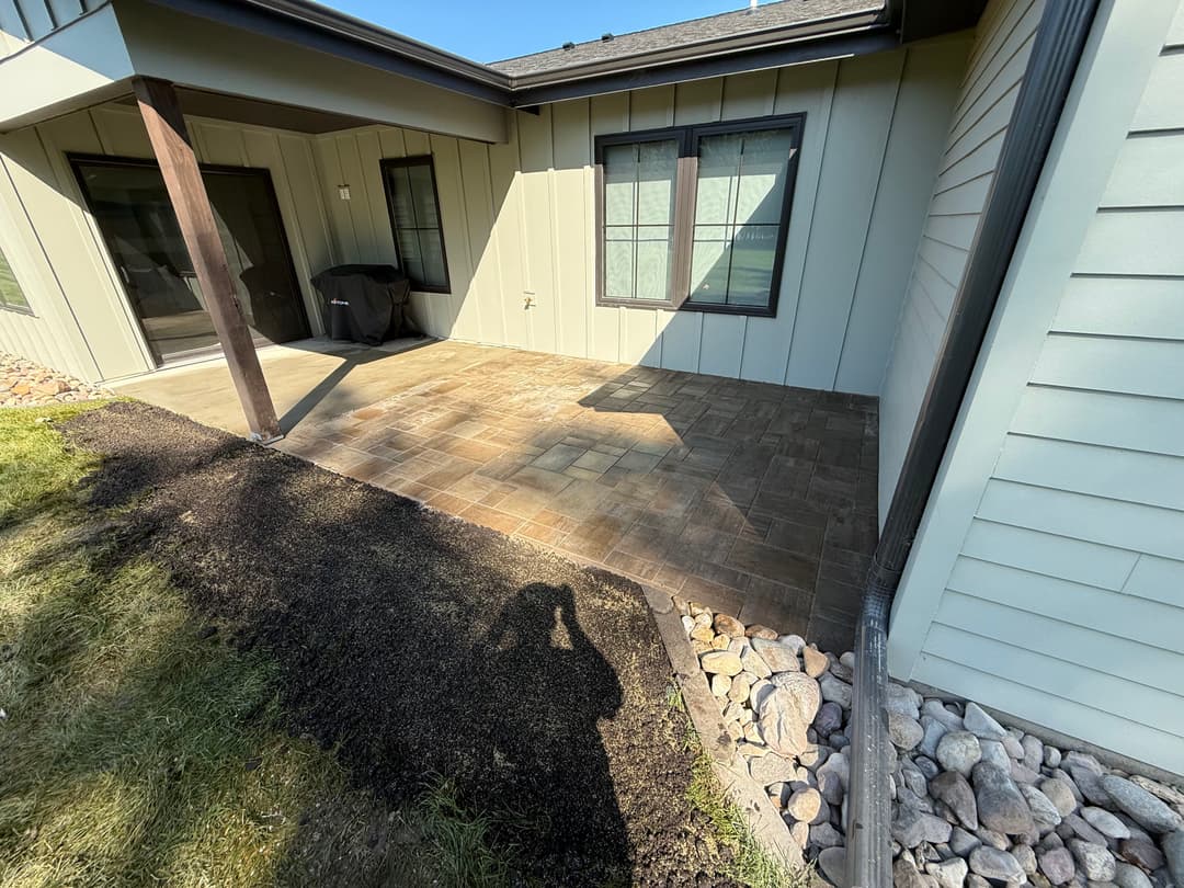 Paver stone patio next to a house with green grass and gravel border.
