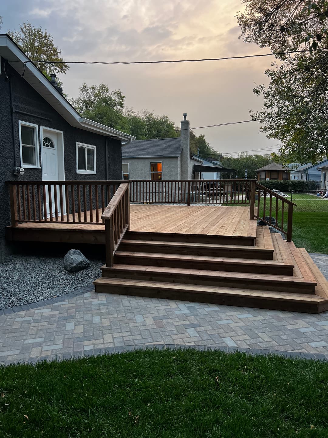New wooden deck with stairs in a residential backyard, surrounded by grass and pathways.