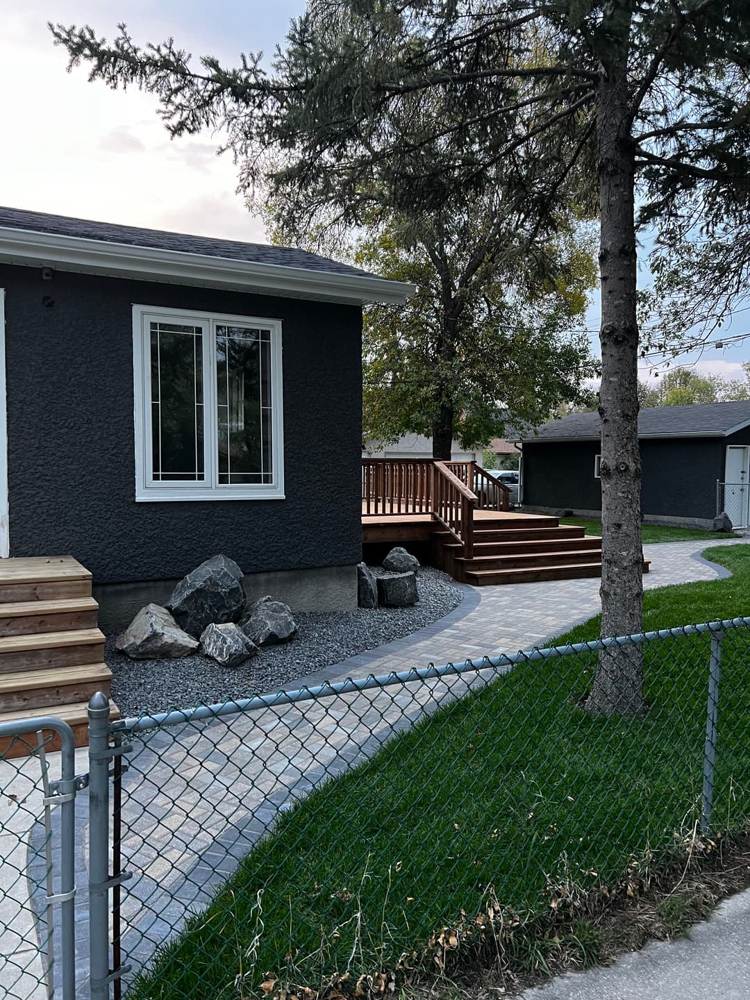 Modern home exterior with wooden deck, stone pathway, and landscaped yard.