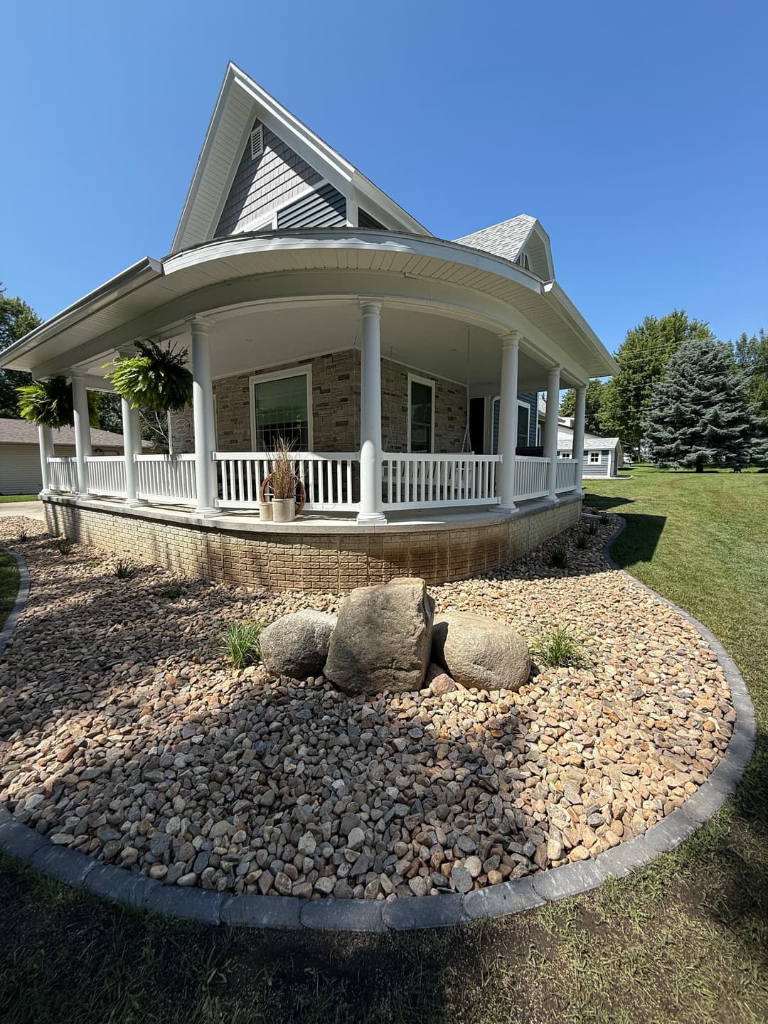 Charming house with a porch, stone landscaping, and lush green yard under a clear blue sky.