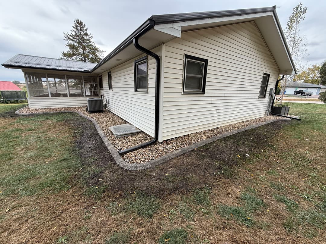 Single-story house exterior with a gravel border and grassy yard, cloudy sky above.