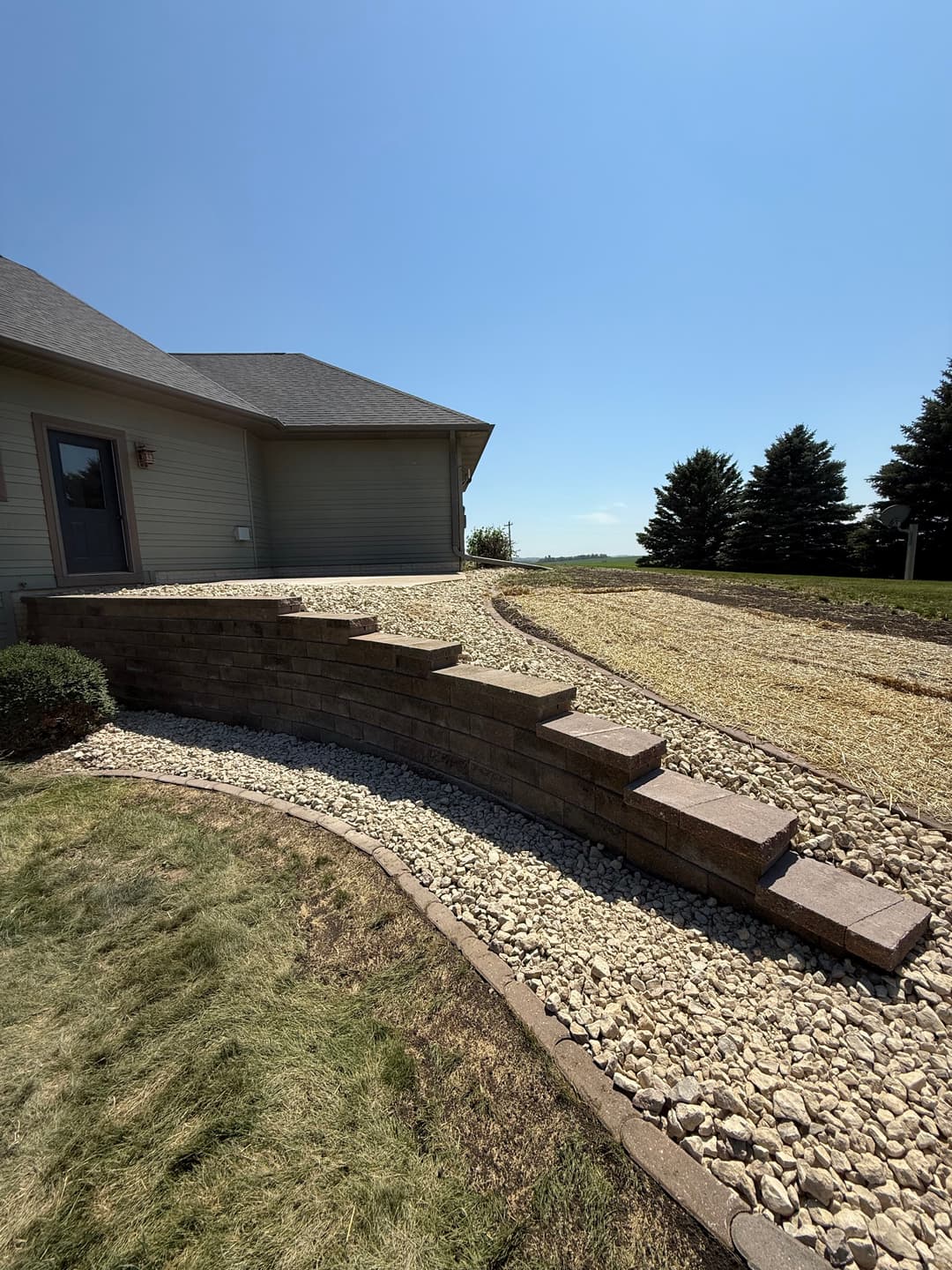 Curved stone steps leading to a house, surrounded by gravel and green grass under a clear sky.