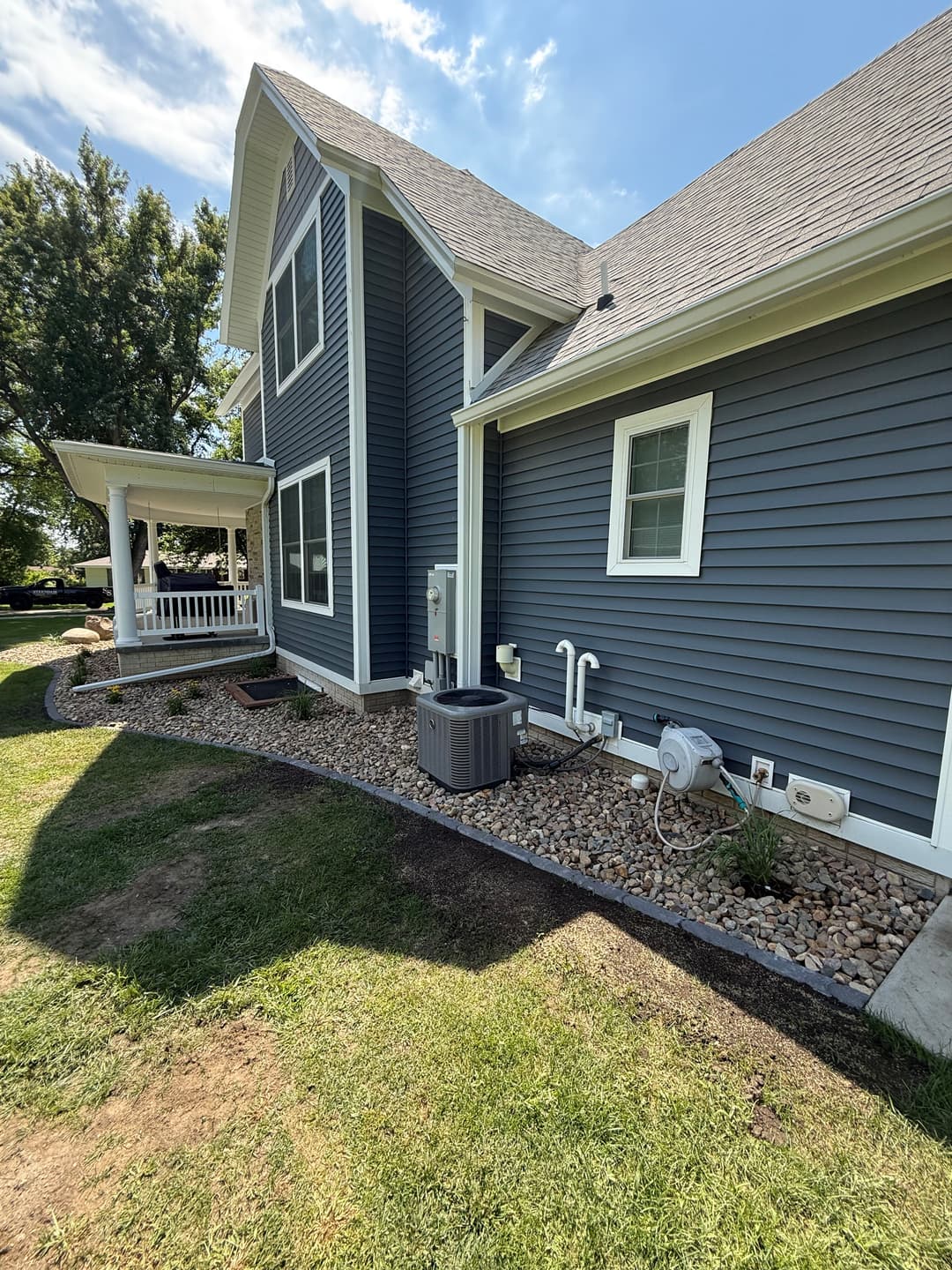 Side view of a modern gray house featuring landscaped garden and porch. Sunny day with blue sky.