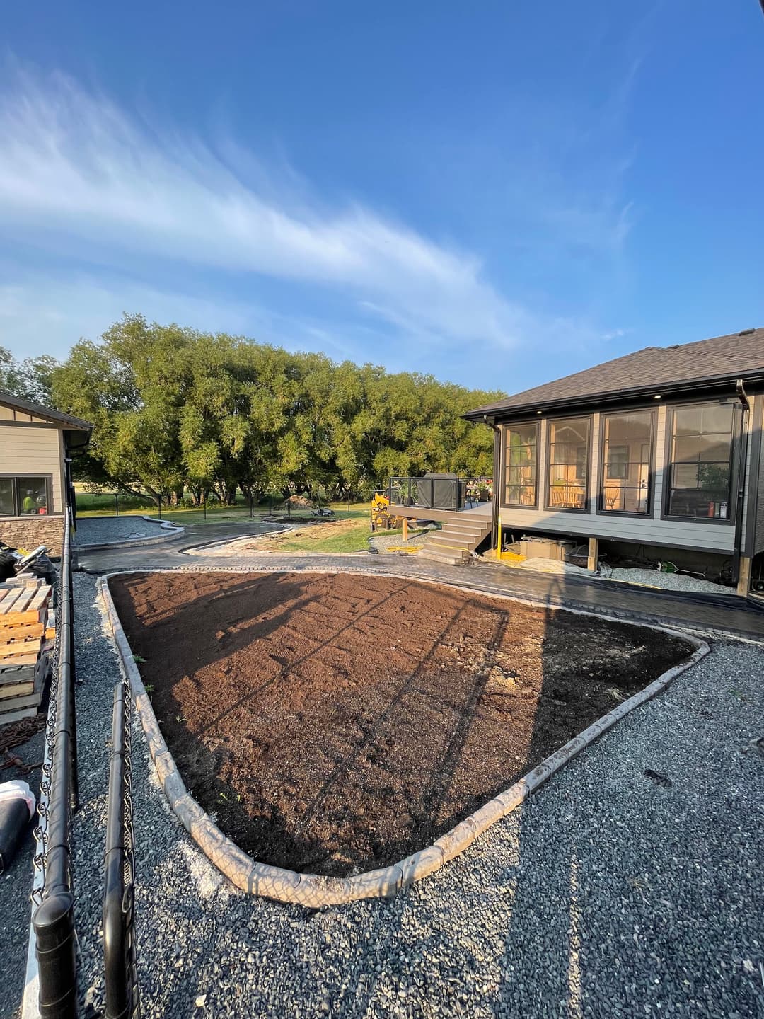 Sunlit garden plot ready for planting, surrounded by gravel paths and nearby house structures.
