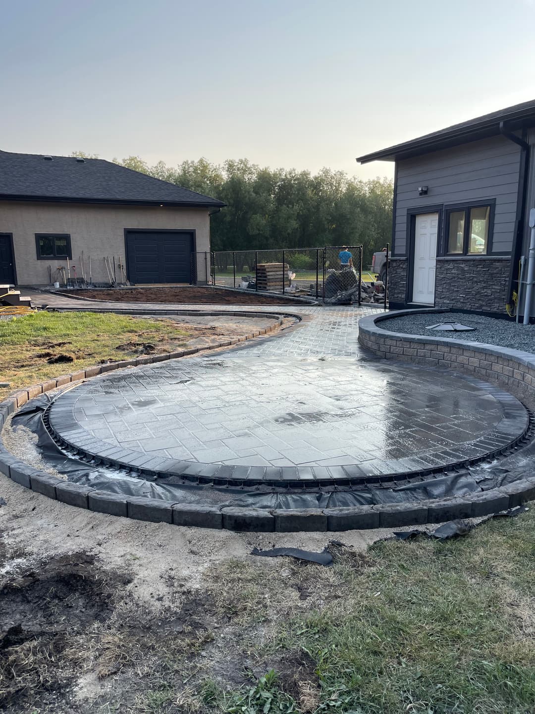 Newly poured concrete patio with circular design and surrounding landscaping under construction.