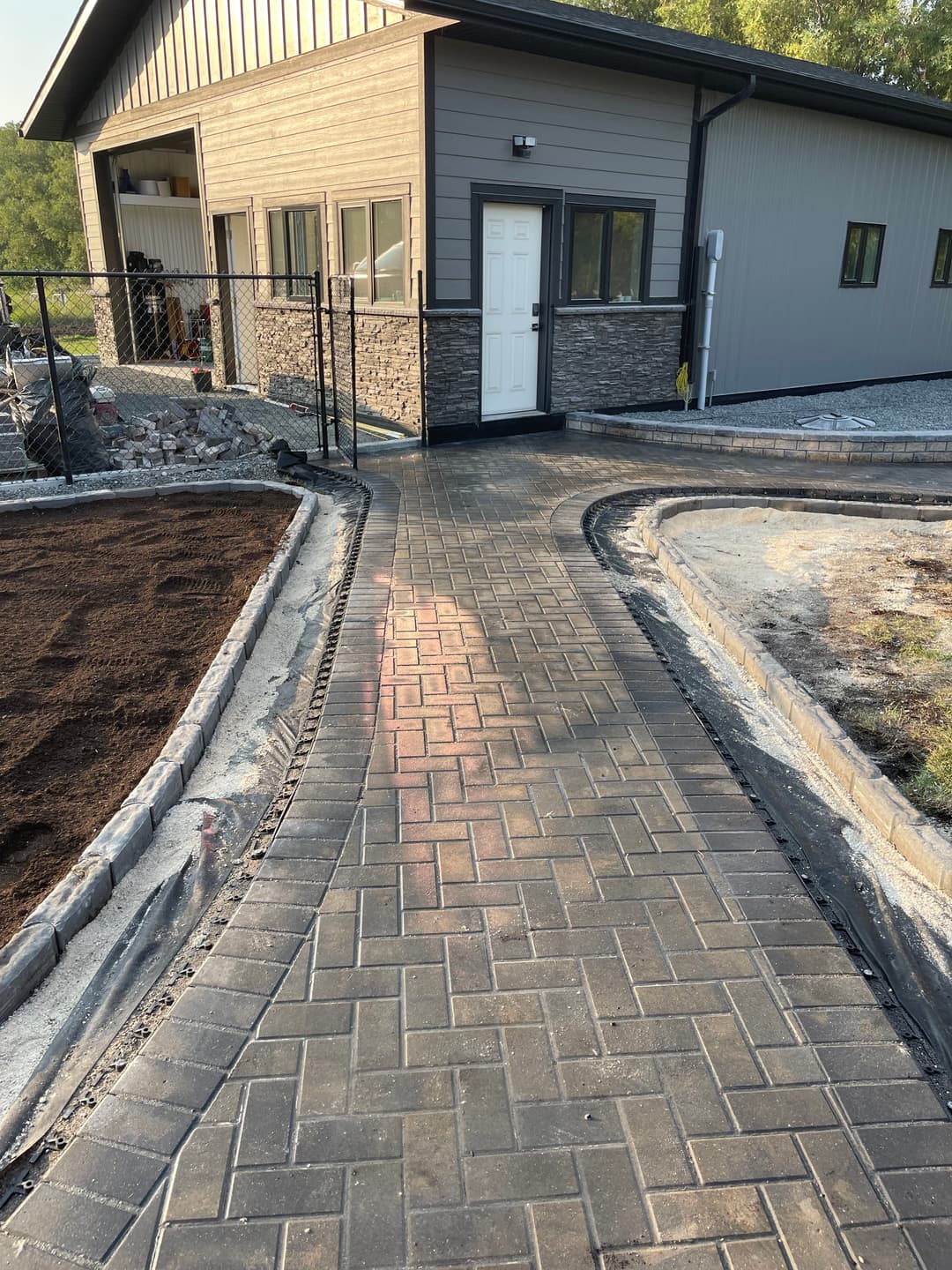 Paved walkway leading to a modern building with stone accents and surrounding landscaping.