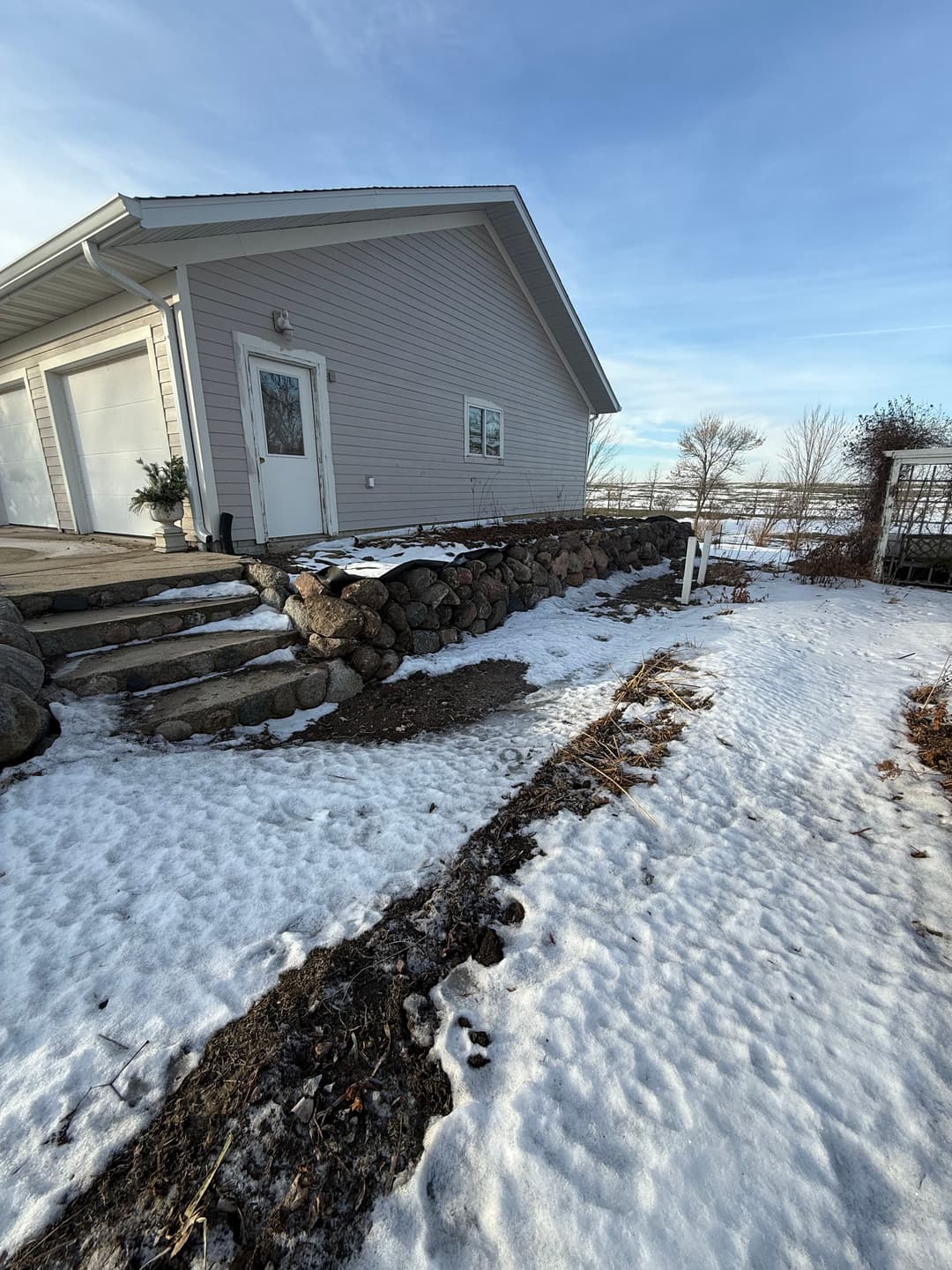 Snow-covered landscape with a modern house, stone steps, and clear blue sky.