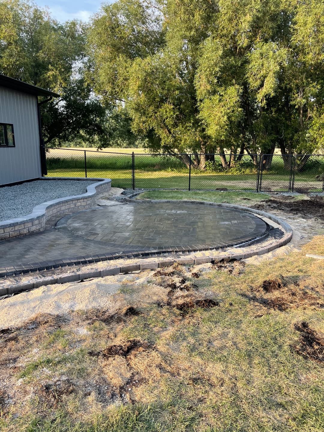 Newly installed brick patio surrounded by grass and trees, near a fenced yard.
